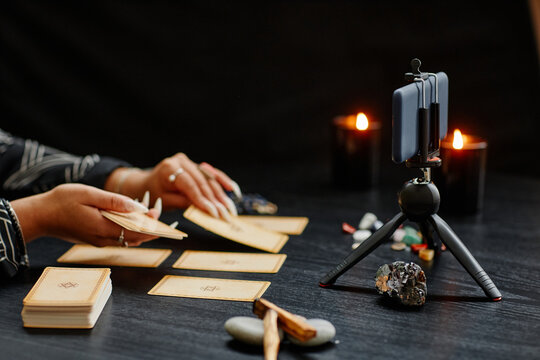 Side view close up of woman doing tarot reading on camera and recording video with smartphone