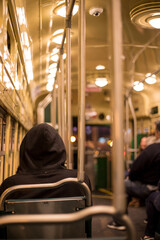 Fototapeta premium A men with his hood on his head inside a bus at night sitting alone. A retro bus with circular lights. Nighttime. Lonely hooded man in a bus.