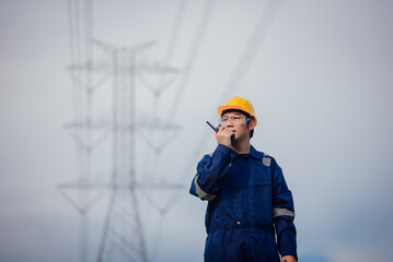 A male power engineer in a yellow helmet inspects the power line under a high voltage electrical...