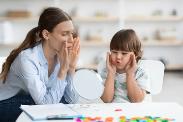 Cute little boy with speech problems practicing with therapist, doing practice and looking at mirror, free space