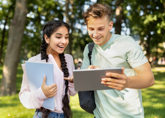 University lifestyle concept. Student guy showing digital tablet to girlfriend, looking at test results outdoors