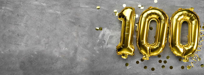 Yellow foil balloon number, number one hundred on a concrete background. Greeting card with the...