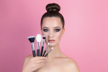 Makeup of a girl's face close-up in the studio on a pink background in the hands of a brush and paint. A young girl does makeup in the studio, paints eyelashes, eyebrows, lips look in the mirror.