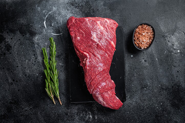 Raw American Tri Tip beef steak on marble board. Black background. Top view