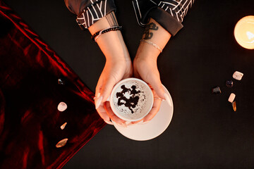 Top down view of female fortune teller holding coffee cup in hands and reading grounds in seance