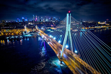 Fototapeta na wymiar Beautiful panoramic aerial drone skyline view of the center of night Warsaw with skyscrapers in the background with the Swietokrzyski suspension bridge - the lights of the big city by night, Poland