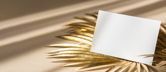Invitation card mockup with golden palm leaves on beige pastel background. Top view, flat lay, copy...