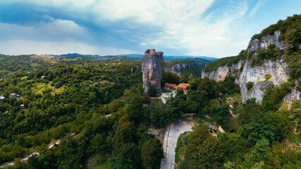 Naklejka premium Wide aerial panorama. Katskhi pillar. Georgian landmarks. Man's monastery near the village of Katskhi. The orthodox church and the abbot cell on a rocky cliff. Imereti, Georgia.vTravel and tourism