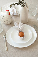 Fototapeta na wymiar Easter table setting with Easter egg in rabbit napkin on plate and cutlery.