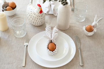 Easter table setting with egg in Easter bunny napkin on plate. Easter table serving.