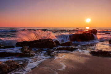 Pastel sunrise over the rocky sea beach. Motion blur