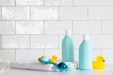 Toiletries baby on tile background. Baby shower gel and shampoo bottle with toy, towel and yellow...