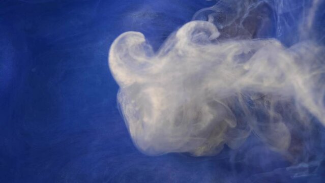 White ink spreading in water on a blue background. Colored acrylic cloud abstract smoke background. Glitter fluid motion. 