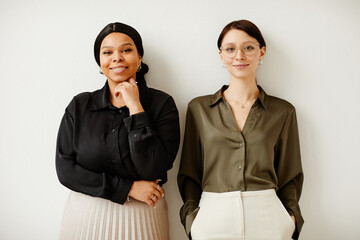 Minimal portrait of two young successful business women smiling with joy while standing against...