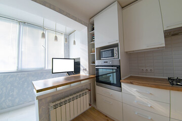 interior of the kitchen and work area with a computer and an armchair on the balcony, loggia. Table top made of solid wood.