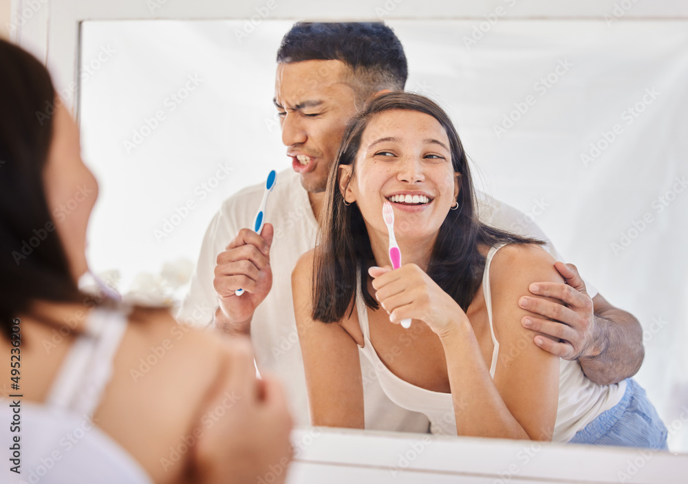 Poster He has to make brushing his teeth a performance. Shot of a happy young couple standing together in their bathroom and feeling playful while brushing their teeth.