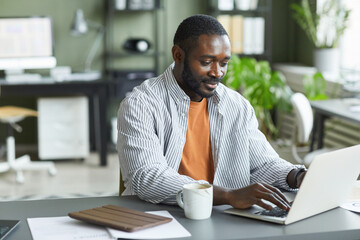 Obraz premium Portrait of adult black man working at home office and using laptop, copy space