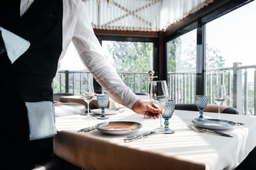 A young waiter in a stylish uniform is engaged in serving the table in a beautiful gourmet restaurant close-up. Table service in the restaurant.