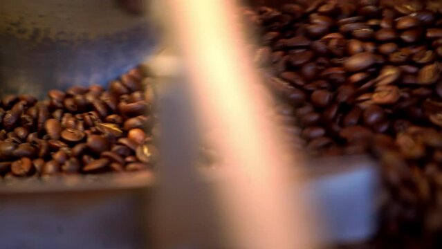 Roasted coffee beans fly and spin on a black background in slow motion. Production of fresh fried coffee beans roasting factory process. Prepared coffee beans mixing around on a cooling plate of oven.