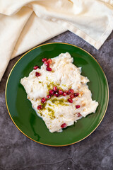 Gullac dessert on dark background. Traditional Ramadan dessert. Güllaç dessert decorated with pistachio and pomegranate. Turkish cuisine delicacies. Top view