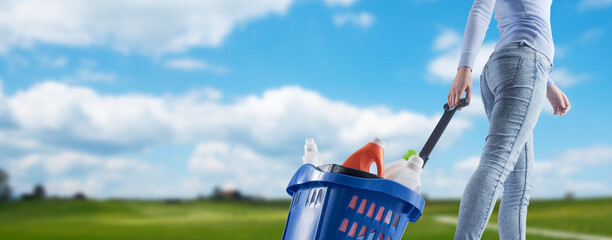 Woman pulling a shopping basket full of cleaning products and green landscape in the background