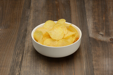 Patatas fritas o chips en un bol de cerámica blanca sobre fondo la mesa marrón