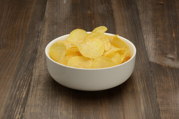Patatas fritas o chips en un bol de cerámica blanca sobre fondo la mesa marrón - obrazy, fototapety, plakaty