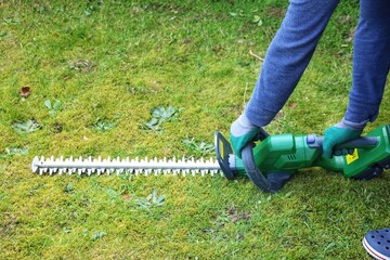 A gardner taking a hedge trimmer from ground for cutting bushes.