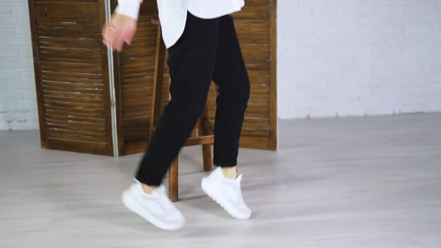 Model jumping high to show white spot shoes. Demonstrating comfortable footwear for everyday activity. Folding screen and tabouret at backdrop.