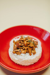 Risotto with mushrooms in a red plate over white background, top view
