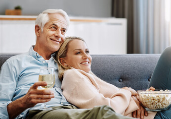 Turning home into their very own cinema. Shot of a happy mature couple relaxing together with wine...