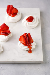 Mini-pavlova with fresh strawberries and red jam - delicious meringue cakes on marble board on...