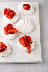 Mini-pavlova with fresh strawberries and red jam - delicious meringue cakes on marble board on...