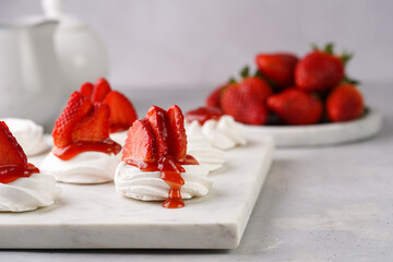 Mini-pavlova with fresh strawberries and red jam - delicious meringue cakes on marble board on off-white background