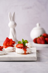 Mini-pavlova with fresh strawberries and red jam - delicious meringue cakes on marble board on off-white background, easter bunny