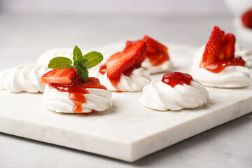 Mini-pavlova with fresh strawberries and red jam - delicious meringue cakes on marble board on off-white background