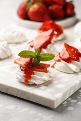 Mini-pavlova with fresh strawberries and red jam - delicious meringue cakes on marble board on...