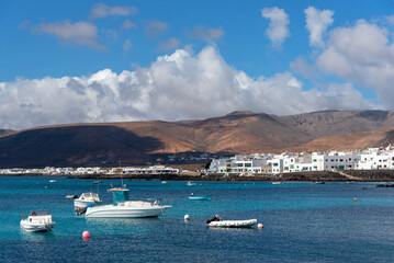 costa de Punta Mujeres en Lanzarote en las Islas Canarias. Yate y barcos varados en un mar turquesa con casa blancas de fondo y montes volcánicos. Naturaleza y paisaje canario. 