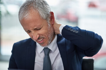 The aches and pains of office work. Shot of a mature businessman suffering from neck pain while working in an office.