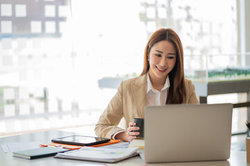 Smiling beautiful Asian businesswoman working on laptop and documents in financial accounting concept office