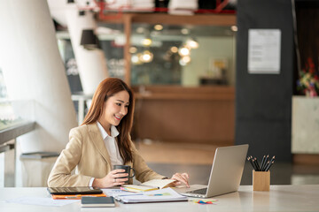 Smiling beautiful Asian businesswoman working on laptop and documents in financial accounting...