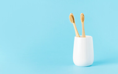 Natural bamboo toothbrushes in a ceramic glass on a blue background. Eco-friendly, zero-waste concept
