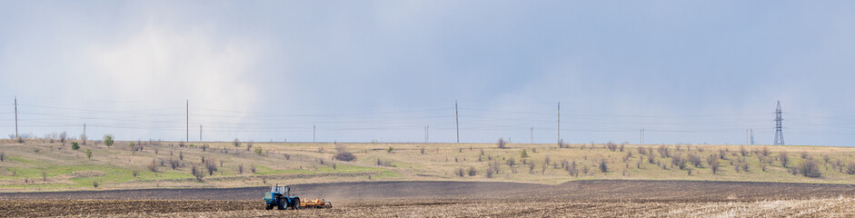 Fototapeta na wymiar Tractor Plowing Field and Tillage. Agricultural land and Farm. Agriculture. Preparing the soil for sowing. Plow Machine Working Season. Panoramic banner.