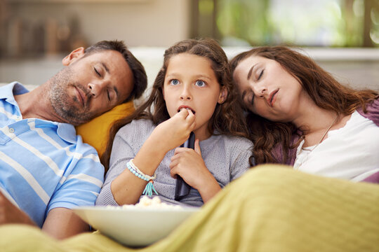 Family movie night. Shot of a girl sitting on the living room watching a movie with her parents asleep beside her.