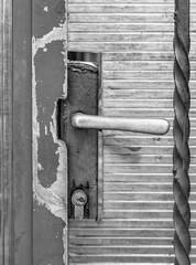 Monochrome picture with an old doorknob on a metal worn out door.