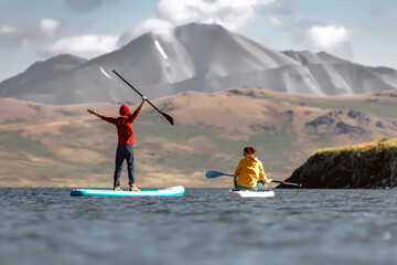 Two happy girls walking on paddle boards at mountain lake