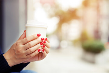 female hand holding paper cup of take away drinking coffee on city background. space place for your text or logo.