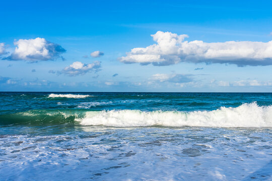 White foamy wave on the beach of the Atlantic Ocean in the spring in Melbourne Beach, Florida. Blue sky with white clouds