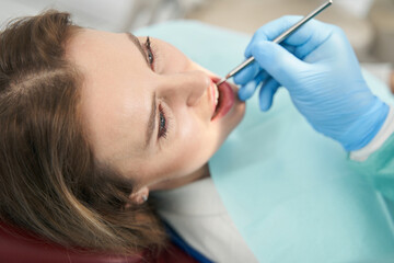 Dentist checking woman teeth with dental mirror