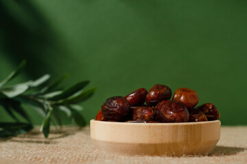 dried dates in a wooden plate on a green background on a sunny day.